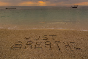 In the picture a beach at sunset with the words on the sand "Just breathe".